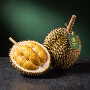 Musang King durian cut open beside a whole fruit with a Duri Gold tag on its stem